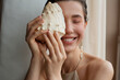 © Amor Burakova/Stocksy - Happy woman hides her eye with a seashell