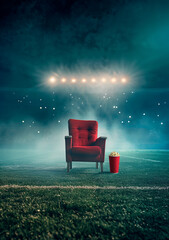 Wall Mural - A red cinema chair on the football field under stadium lights, popcorn and drink cup in front of it, foggy night atmosphere, cinematic lighting, hyper realistic photography


