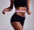 © peopleimages.com - Studio, fitness and black woman with tape for diet, health and wellness by mockup space. Female model, tracking and measure waist for progress, body goals results and benefits by gray background