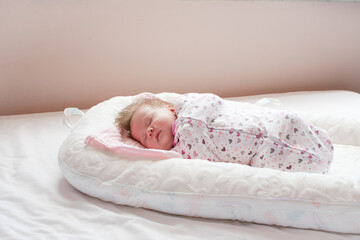 Swaddled Caucasian Newborn baby sleeping in a baby lounger. Baby nest.