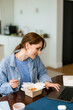 © DZ FILM/Stocksy - A woman eats a wok and uses a laptop