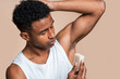 © nomad studio/Stocksy - African american man in a white tank top applying stick deodorant