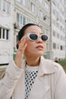 © Azamat Mukanov/Stocksy - Woman in sunglasses against the background of an apartment building