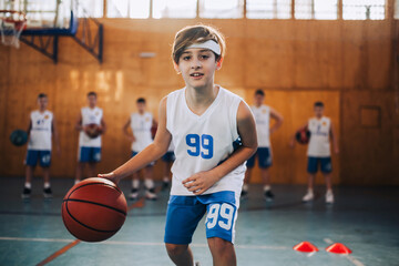 Poster - A junior basketball player dribbling a ball on training at indoor court.