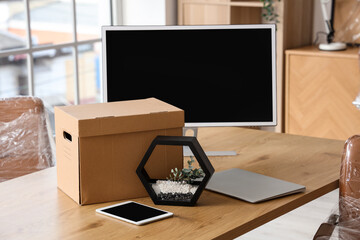 Wall Mural - Desk with tablet computer, laptop, PC monitor and cardboard box in office on moving day