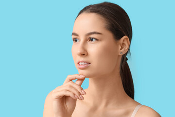 Poster - Young woman with hand near her face on blue background. Nose plastic surgery concept