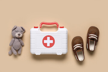 Toy first aid kit with kid's shoes and teddy bear on beige background. Top view