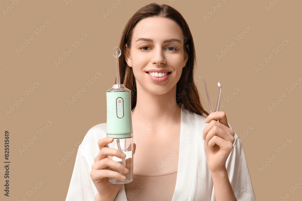 Happy young woman with oral irrigator on brown background