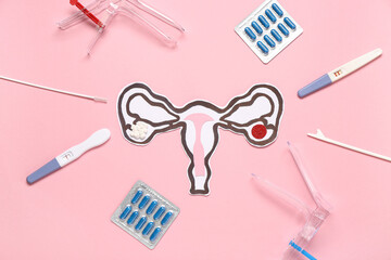 Wall Mural - Paper uterus with gynecological speculums, pills and pap smear test tools on pink background