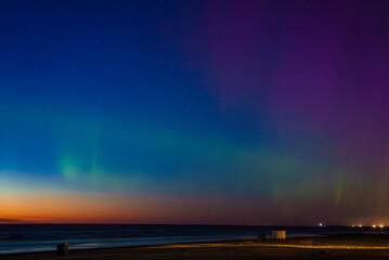 Stunning display of the aurora borealis over a beach in Riga and Jurmala, Latvia. Vibrant green, blue, and purple hues illuminate the night sky, contrasting with the dark horizon.
