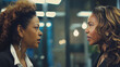 © Ron - two black women in their late thirties, one with curly hair and the other with straight hair, wearing business attire facing each other having an argument inside a modern office building
