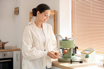 Poster - Beautiful young happy woman cup of cappuccino and modern coffee machine in kitchen