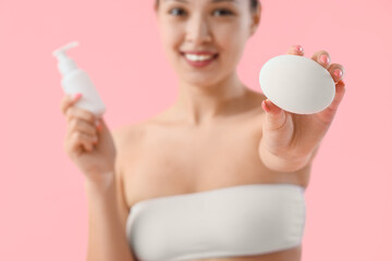 Poster - Young Asian woman with soap and cream on pink background, closeup