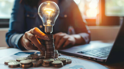 Poster - Hand stacking coins under a glowing lightbulb, symbolizing the concept of inflation and economy