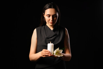 Wall Mural - Young woman with funeral lily flower and burning candle on black background