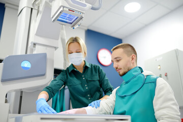 Wall Mural - Female radiologist going to made x-ray shot of young man hand in x-ray room in modern clinic. Patient wearing in protect lead apron