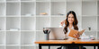© Satori Studio - A woman sitting at a desk with a laptop and a notebook. She is smiling and holding a pen. The scene suggests a productive and positive work environment