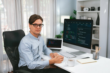 IT developer looking camera with online software development information on pc and laptop monitor beside, coding program on updated version application project creating new code system. Pecuniary.