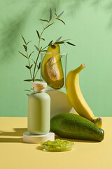 Sample cosmetic bottle in green color placed on a round platform with fresh avocado and yellow banana decorated in back, a dish of chopped avocado placed in front. Green background photo, front view