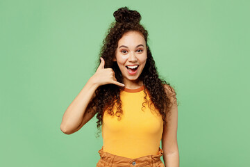 Wall Mural - Young fun woman of African American ethnicity wear yellow tank shirt top doing phone gesture like says call me back isolated on plain pastel light green background studio portrait. Lifestyle concept.