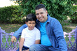 © Arlette - Divorced single dad on a park bench with his 10-year-old dark-skinned Latino son spending quality time and celebrating Father's Day