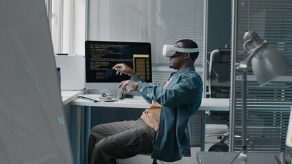 Wall Mural - side view medium shot of young black man wearing vr headset making hand gestures in air while testin