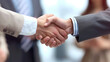 © nopommajun - Two well-dressed professionals shaking hands in a business context with other colleagues in soft focus behind them