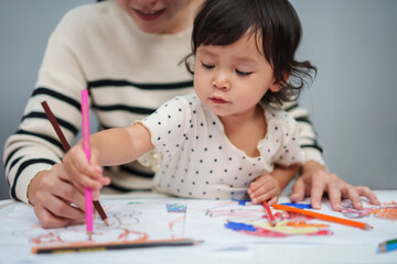 Wall Mural - toddler baby training to drawing with colored pencil with mother helping on table