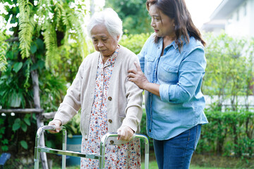 Caregiver help Asian elderly woman disability patient walk with walker in park, medical concept.