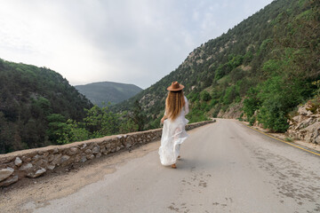 Wall Mural - A woman in a white dress is walking down a road with a hat on
