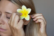 © Марина Демешко - Cropped shot of a young caucasian woman putting white and yellow frangipani flower in her hair on a dark gray background. Hair ornaments, decorations, beauty concept