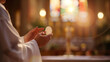 © nopommajun - Close-up of a priest's hands holding a communion wafer with church windows in the background