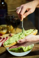 Wall Mural - The process of spreading Guacamole on grilled bread. A dish of avocado and vegetables.