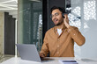 © Tetiana - Indian young man working in the office on a laptop, sitting at the table with headphones and listening to music, relaxing and singing along