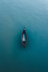 Wall Mural - Aerial view of a single boat floating on a calm, open body of water. Highlight the solitude and minimalist beauty of the scene, with the boat casting a gentle shadow on the surface. 