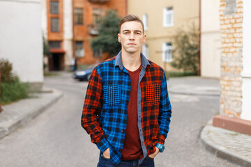 Trendy stylish young man with a hairstyle in a fashionable colored shirt walks on the street