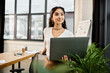 © LIGHTFIELD STUDIOS - Young indian woman standing in office, using laptop.
