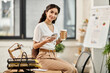© LIGHTFIELD STUDIOS - A young indian woman sits at a desk, elegantly holding a cup of coffee.
