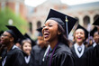 © Cadengo - joyful young black woman in cap and gown laughing, with a crowd of graduates in the background
