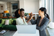 © Marko Geber - Two professional women celebrating success with a high-five in a stylish office
