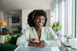 © Marko Geber - Portrait of a smiling young Black woman sitting at a desk in a modern home office