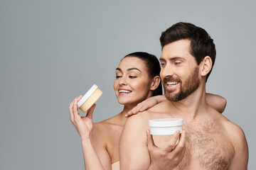 Wall Mural - Jolly couple elegantly hold a jar of cream, showcasing their skincare routine.