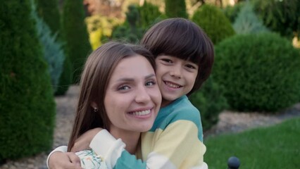 Wall Mural - Little boy hugging his mother in park, camera moving towards them