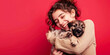 © Creative Content  - Happy woman in a cozy sweater hugging a cute puppy against a red background