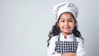 © Kanlayarawit - A cute happy smiling young Indian girl dresses like a chef on a plain white background with copy space for text.
