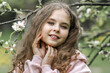 © Светлана  - A beautiful toddler girl in a pink dress stands by a blooming white apple tree in the park and enjoys the beauty of a blooming garden, spring