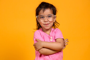 Wall Mural - A young child with a confident smile .The child is wearing a pink shirt and large, clear-rimmed glasses. They have their arms crossed over their chest in a playful and self-assured manner