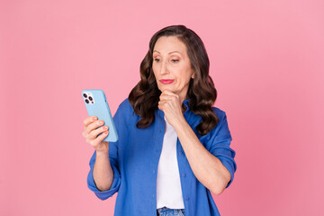 Poster - Photo portrait of lovely senior lady hold device skeptical dressed stylish blue garment isolated on pink color background