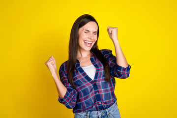 Poster - Photo portrait of attractive young woman winning raise fists dressed stylish plaid clothes isolated on yellow color background