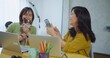 © HarryKiiM Stock - Two Asian women friend are sitting at a table with a small dog. women holds a Chihuahua and smiles for a selfie taking a picture of the dog with cell phone in a bright cozy workspace business home